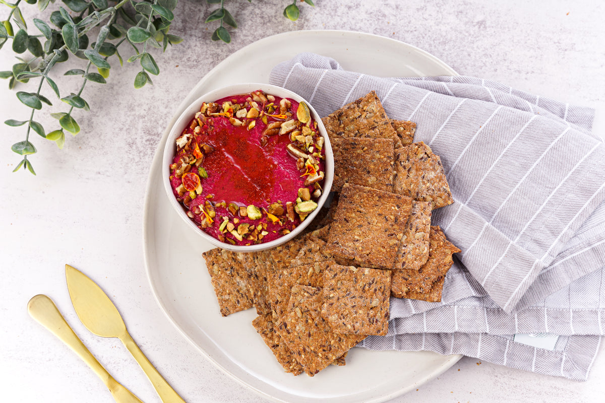 Primal Bakery protein crackers served with a bright beet dip topped with chopped nuts on a plate