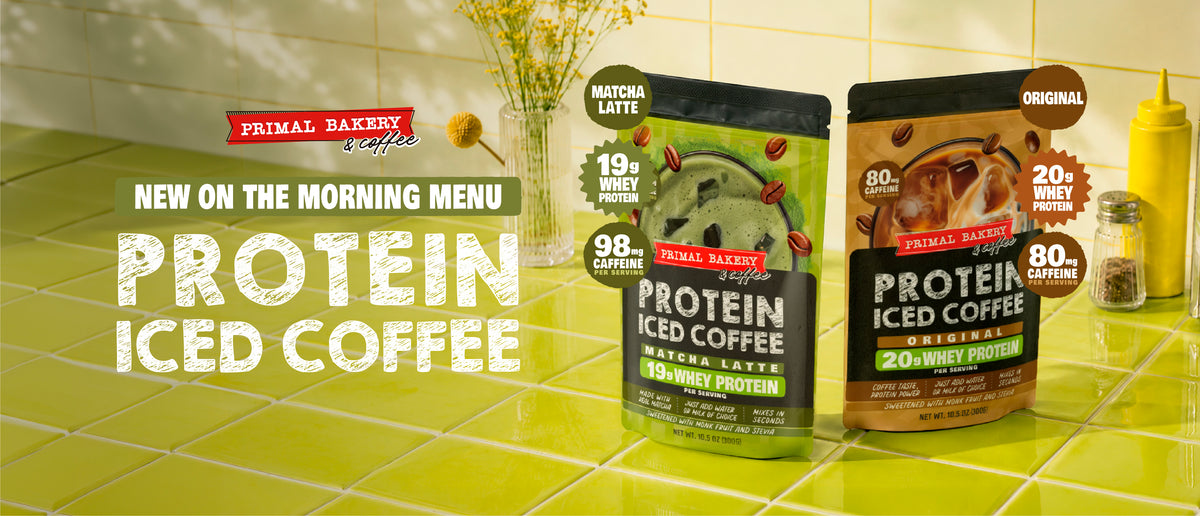 Two pouches of Primal Bakery Protein Iced Coffee on a bright green tiled counter, with one green pouch labeled Matcha Latte and one brown pouch labeled Original. Large text reads 'PROTEIN ICED COFFEE' and 'NEW ON THE MORNING MENU'.