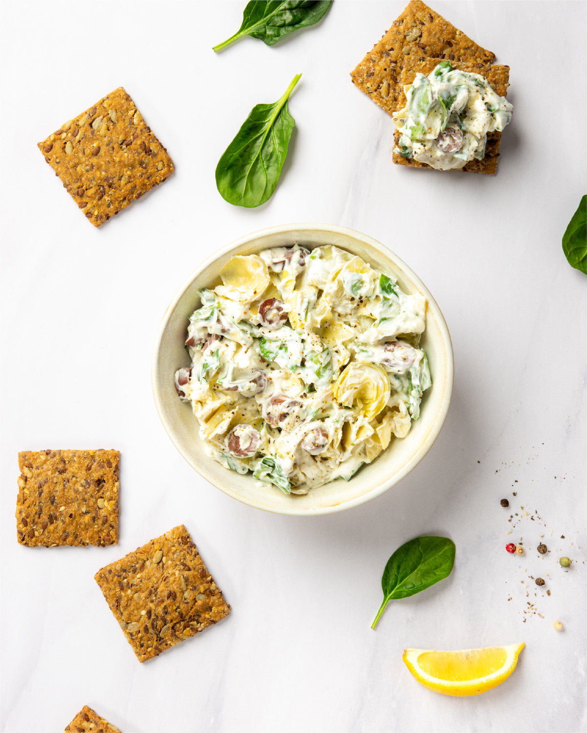 Primal Bakery Protein Crackers served with a creamy spinach and artichoke dip, fresh spinach, and lemon.